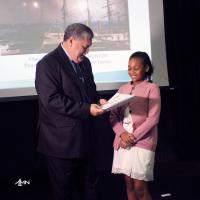 A aluna Gabriele Abreu, representante do primeiro lugar Lucas Bonfim, recebendo o prêmio das mãos do Vice-Almirante José Carlos Mathias, Diretor da DPHDM. 